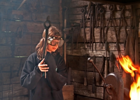 This young modern girl has safety googles on while trying to learn blacksmith skills, with old pioneer tools and a live fire.の写真素材