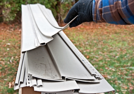 This gloved hand is lifting a piece of vinyl siding, from a stack of vinyl siding on the ground   Examining some materials for home improvement の写真素材