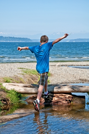 This 13 year old Caucasian boy is running and jumping while playing at the beach   His arms are held high in the air, ready to conquer the world   Full body, rear view in vertical format の写真素材