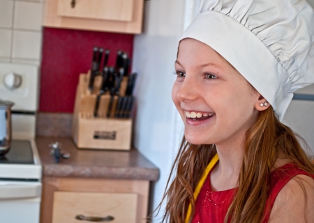 This 10 year old Caucasian girl is happy and smiling in the kitchen, while wearing a white chefの写真素材