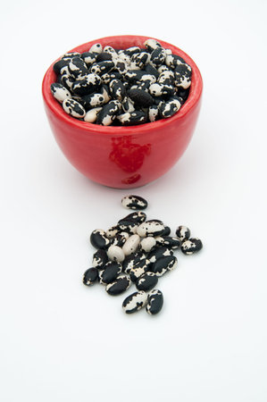 Red bowl of heirloom orca beans, dried legume vegetable on a light background.  Rare bean seeds...