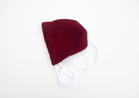 Cranberry colored baby bonnet knit isolated on a light background.  Baby hat has white satin ribbon.