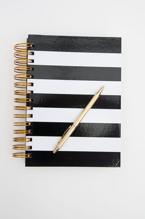 Diary striped black and white book with gold ring binders and a shiny gold pen writing instrument...