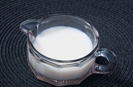 Milk in vintage creamer pitcher, depression era pink glass on a black placemat.  Closeup of beverage for coffee and tea still life.の写真素材