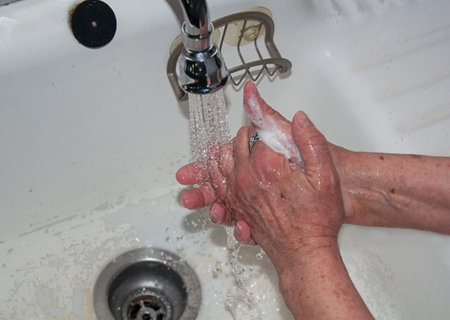 Senior citizen hand washing with soap and running water in sink of an eldery person with disease...