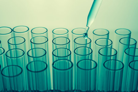 Pipette over laboratory test tube in rack dropping sample chemical for science experiment in lab
