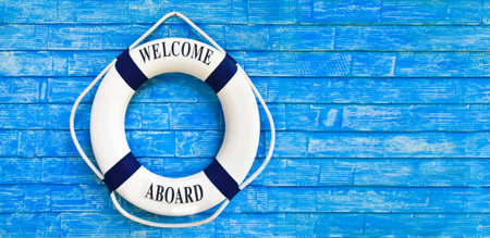 White color Life buoyancy with welcome aboard on it hanging on blue wall. had space on right side...