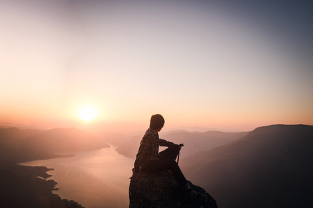 Traveler watching amazing sunset. Silhouette of the young man on the mountainの写真素材