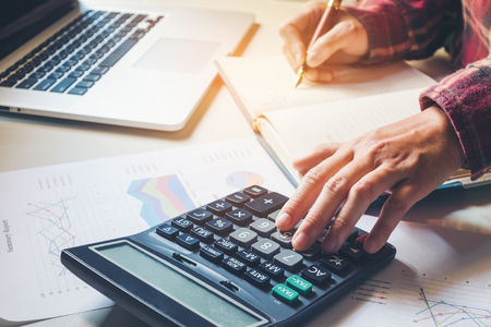 Businessman's hands with calculator at the office and Financial data analyzing counting on wood deskの写真素材