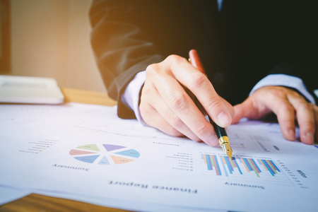 business man holding pen pointing on summary report chartの写真素材