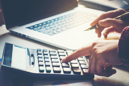 Businessman's hands with calculator and using laptop at the office and Financial data analyzing counting on wood deskの写真素材