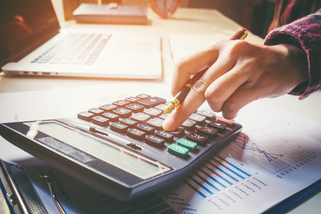 Businessman's hands with calculator at the office and Financial data analyzing counting on wood deskの写真素材
