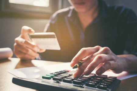 Saving money concept Man hand using calculator and holding credit card shopping online Row and coin stack growing businessの写真素材