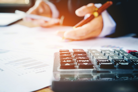 Businessman's hands with calculator at the office and Financial data analyzing counting on wood deskの写真素材