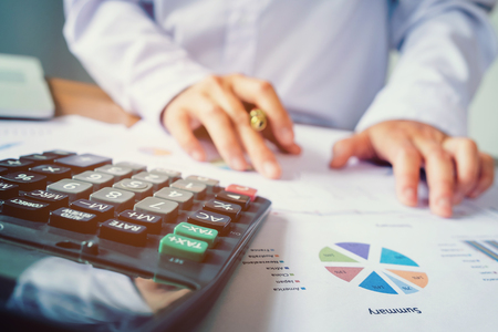 Businessman's hands with calculator at the office and Financial data analyzing counting on wood deskの写真素材