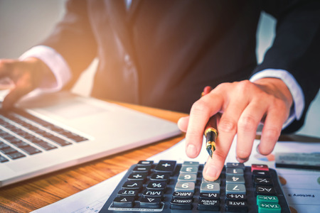 Businessman's hands with calculator at the office and Financial data analyzing counting on wood deskの写真素材