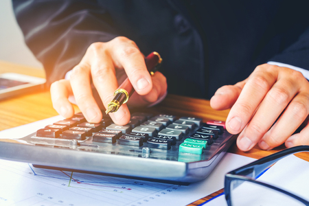 Businessman's hands with calculator at the office and Financial data analyzing counting on wood deskの写真素材