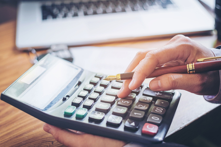 Businessman's hands with calculator and cost at the office and Financial data analyzing counting on wood deskの写真素材