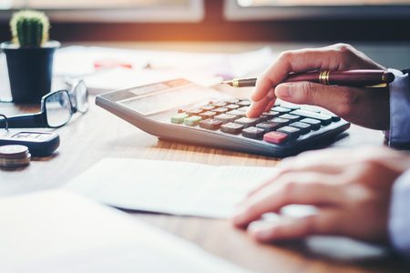 Businessman's hands with calculator and cost at the office and Financial data analyzing counting on wood deskの写真素材