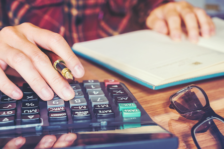 Businessman's hands with calculator counting making notes at homeの写真素材