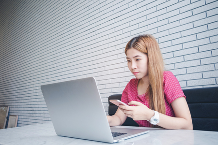 Asian girl working at a coffee shop sitting with mobile phone and laptop. Manager doing job at loft officeの写真素材