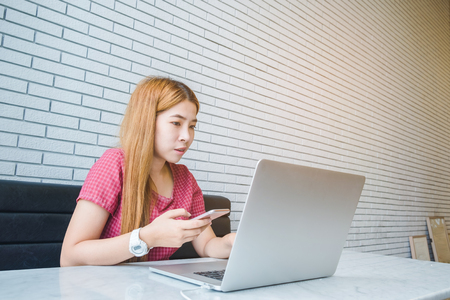 Asian girl working at a coffee shop sitting with mobile phone and laptop. Manager doing job at loft officeの写真素材