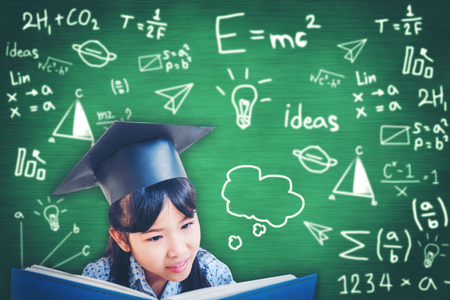 Asian school kid graduate in graduation cap and reading a book   over blackboard.の写真素材
