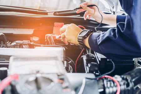 auto mechanic uses a multimeter voltmeter to check the voltage level in a car battery.の写真素材