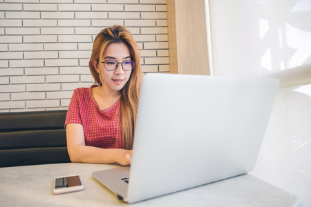 Asian girl working at a coffee shop sitting with mobile phone and laptop. Manager doing job at loft officeの写真素材