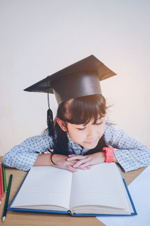 Asian school kid in graduation cap and reading a bookの写真素材