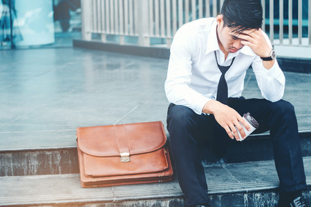 Tired or stressed businessman sitting on the walkway after work outdoor conceptの写真素材