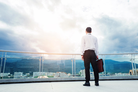 Businessman standing on a roof and looking at city Success and thinking conceptの写真素材