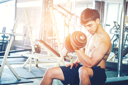 Muscular Man built athlete working out in gym sitting on weightlifting machine and lifting dumbbellの写真素材