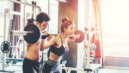 Sport girl doing weight exercises  working with heavy barbells  her personal trainer at Gym workoutの写真素材