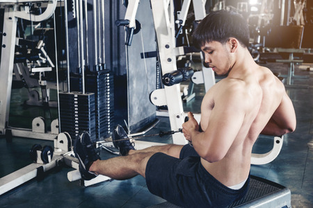 Fitness young man exercising using rowing machine in the gymの写真素材
