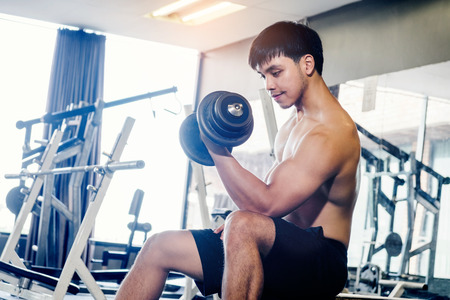 Muscular Man built athlete working out in gym sitting on weightlifting machine and lifting dumbbelの写真素材