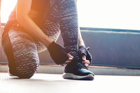 Young woman tying her shoelaces before exercise in gymの写真素材