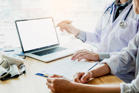 Doctor consulting with patient presenting results on blank Screen tablet computer sitting at tableの写真素材