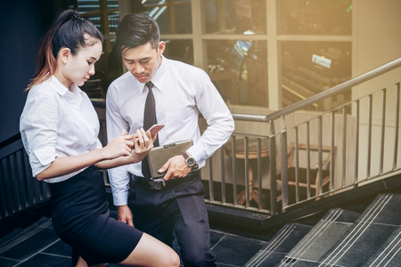 Business man and woman Using smartphone standing talking and viewing documents outdoorの写真素材