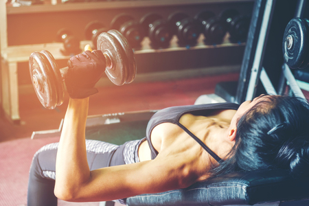 Asian sports woman doing exercises with dumbbell weights in gymの写真素材