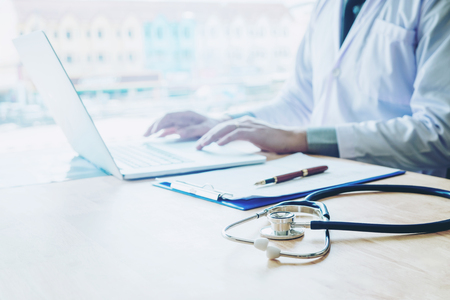 Doctor typing information on Laptop in Hospital office focus on Stethoscopeの写真素材