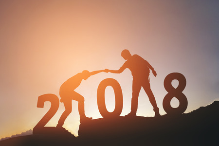 Friend hiking help each other silhouette in 2018 new year on mountainsの写真素材