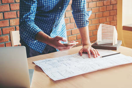 Architect or engineer using smart phone working in office on blueprint. Architects workplaceの写真素材