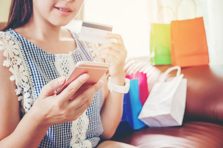 Woman shopping online using smartphone with credit card enjoying in homeの写真素材