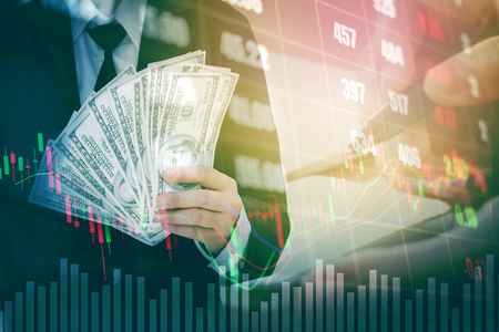 Businessman Holding money US dollar bills on digital stock market financial exchange information and Trading graph backgroundの写真素材