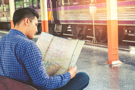 Tourist man backpacker using map to travel at train stationの写真素材
