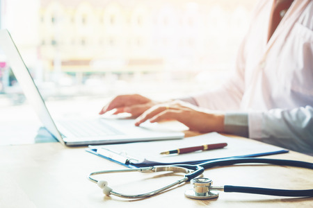 Doctor typing information on Laptop in Hospital office focus on Stethoscopeの写真素材