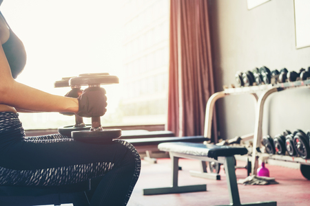Asian sports woman doing exercises with dumbbell weights in gymの写真素材
