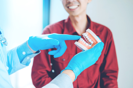Dentist talking to smiling male patient and showing denture in dental officeの写真素材