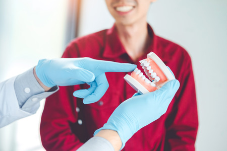 Dentist talking to smiling male patient and showing denture in dental officeの写真素材
